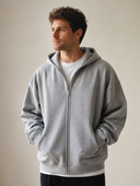 Man draagt grijze oversized zip hoodie met capuchon, driekwartzicht